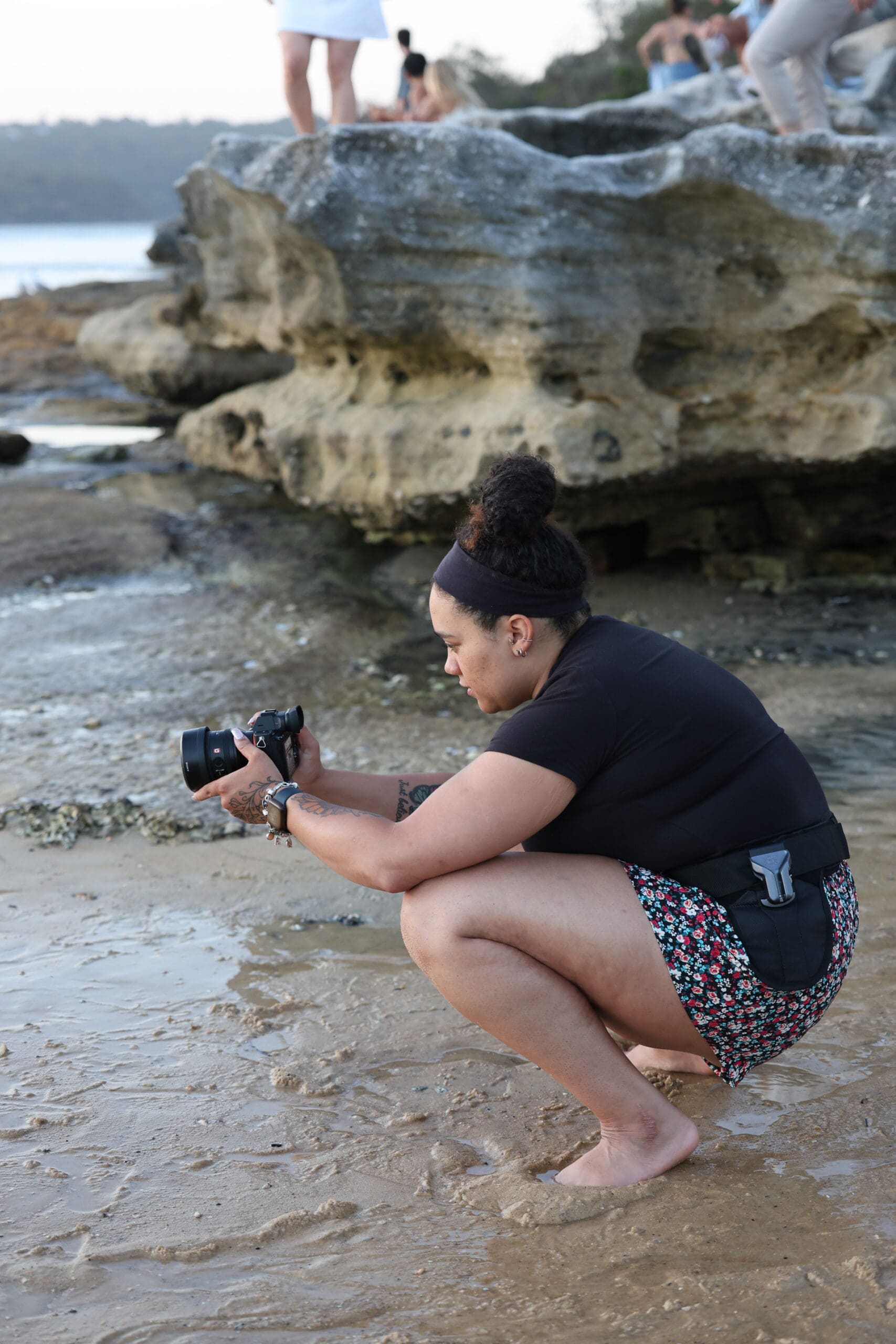 Mary Edelkind working at Milk Beach in Sydney, NSW wearing a Spider Holster belt system, capturing candid moments during a coastal photoshoot with ocean views and natural light.